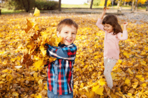 Two young children playing with fallen leaves in a sunny park.